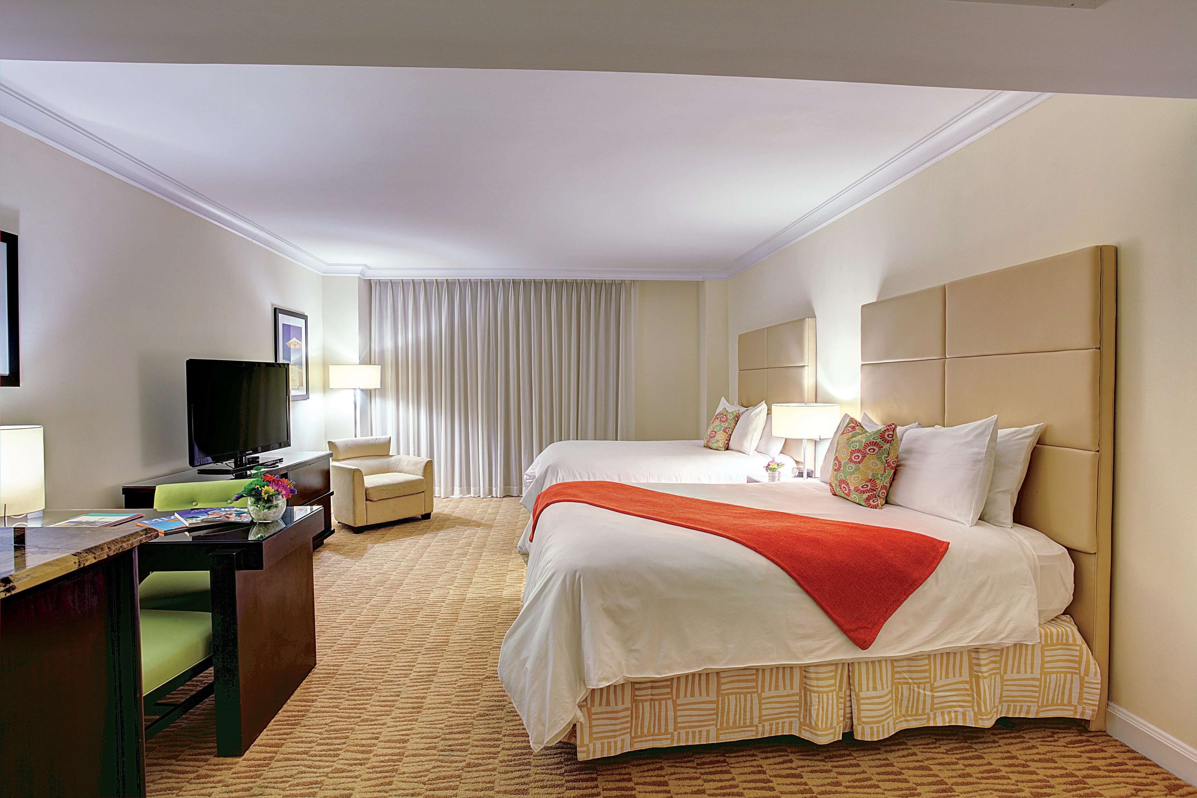 Ein Hotelzimmer mit einem großen Bett, einem Schreibtisch mit Computer, einem Fernseher und einem Sessel.