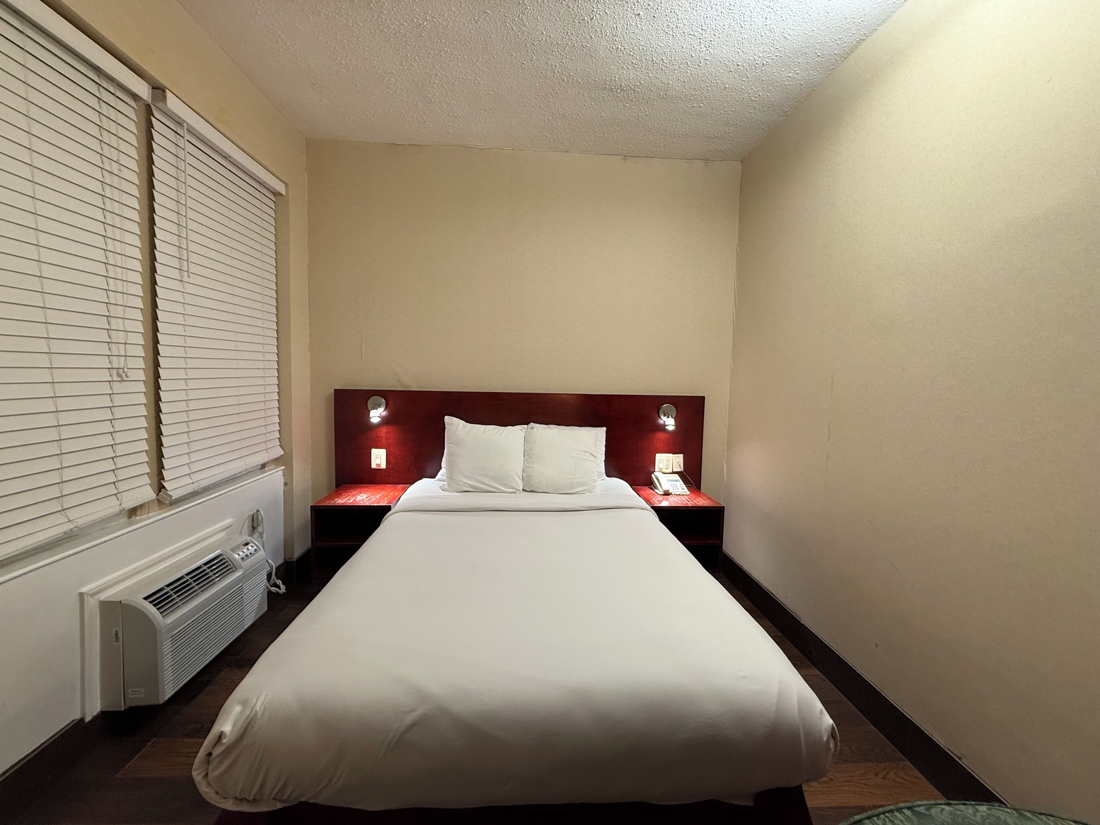 A hotel room with a single bed, a nightstand with a telephone, and a wall-mounted heater.