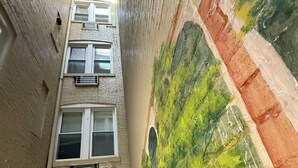 A narrow corridor with a mural on one wall, a staircase, and a piano in the distance. - Windsor Inn Hotel (Washington)
