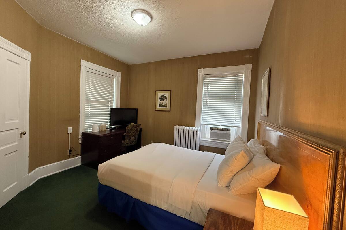 A bedroom with a bed, a desk, a television, and a radiator.