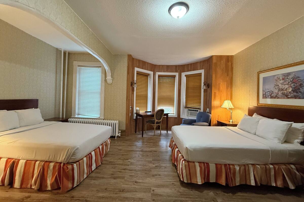 A hotel room with two beds, a desk, and a chair.