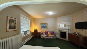 A hotel room with a bed, a sofa, a fireplace, a television, and a framed picture on the wall. - Windsor Inn Hotel (Washington)