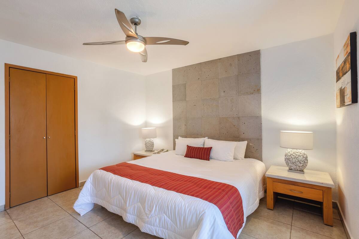 A bedroom with a bed, nightstands, a ceiling fan, and a wooden wardrobe.