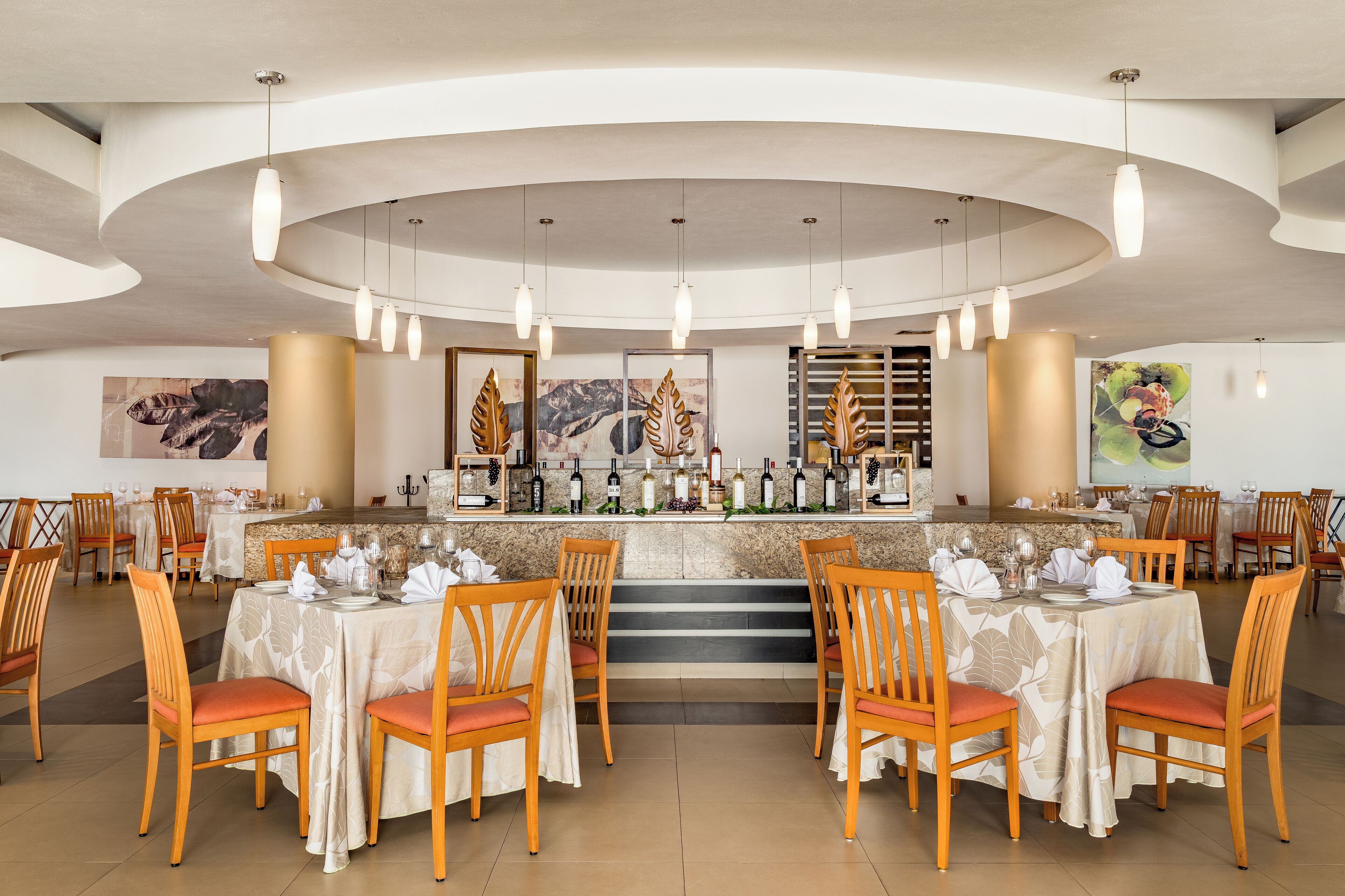 A restaurant with a curved ceiling, multiple dining tables with chairs, a bar area with a wine display, and artwork on the walls.