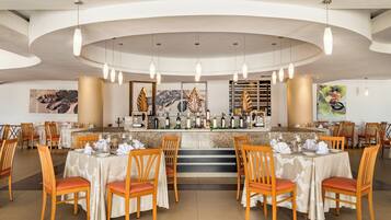 A restaurant with a curved ceiling, multiple dining tables with chairs, a bar area with a wine display, and artwork on the walls.