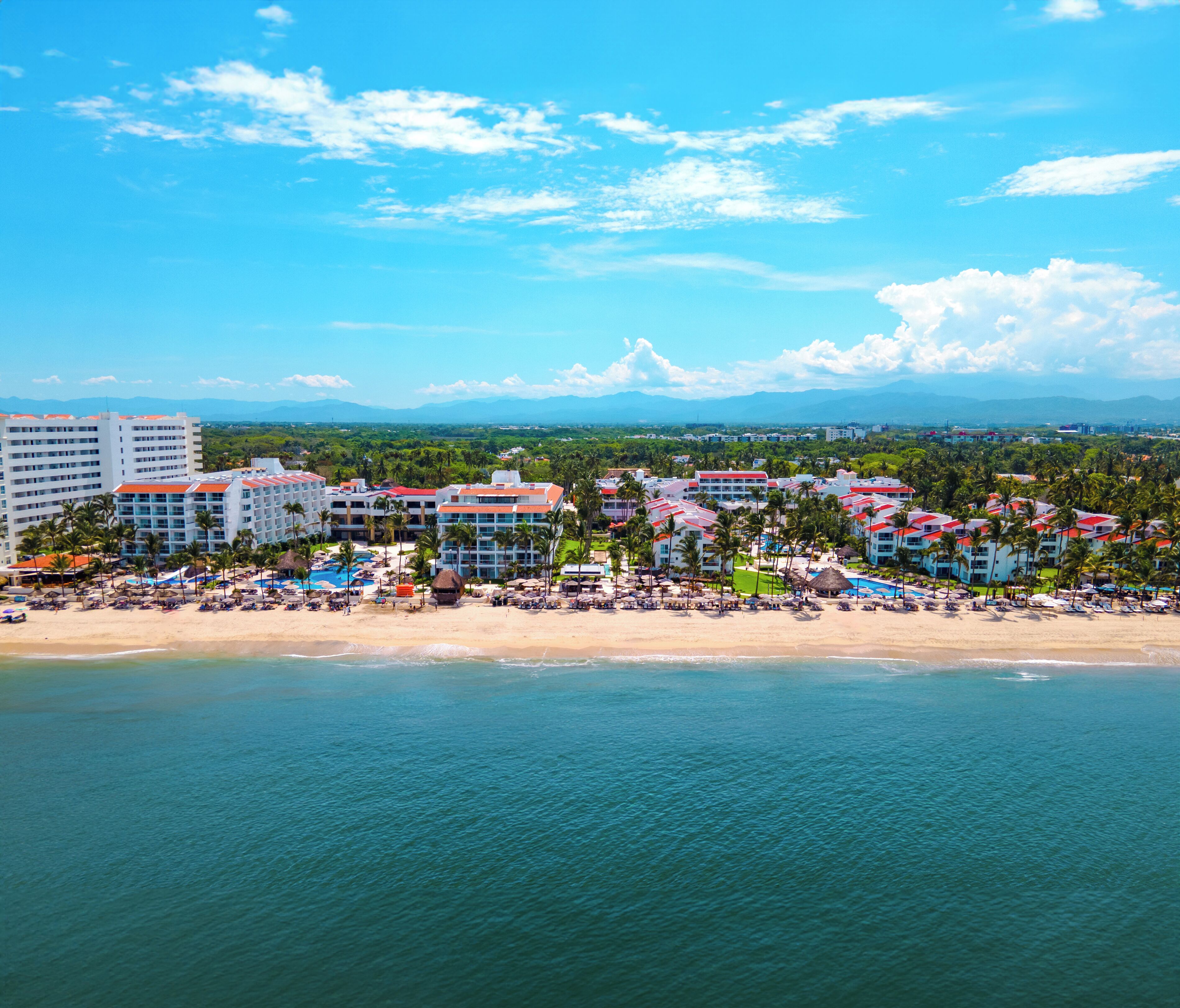 A resort with multiple buildings, a beach, and a view of mountains in the distance.