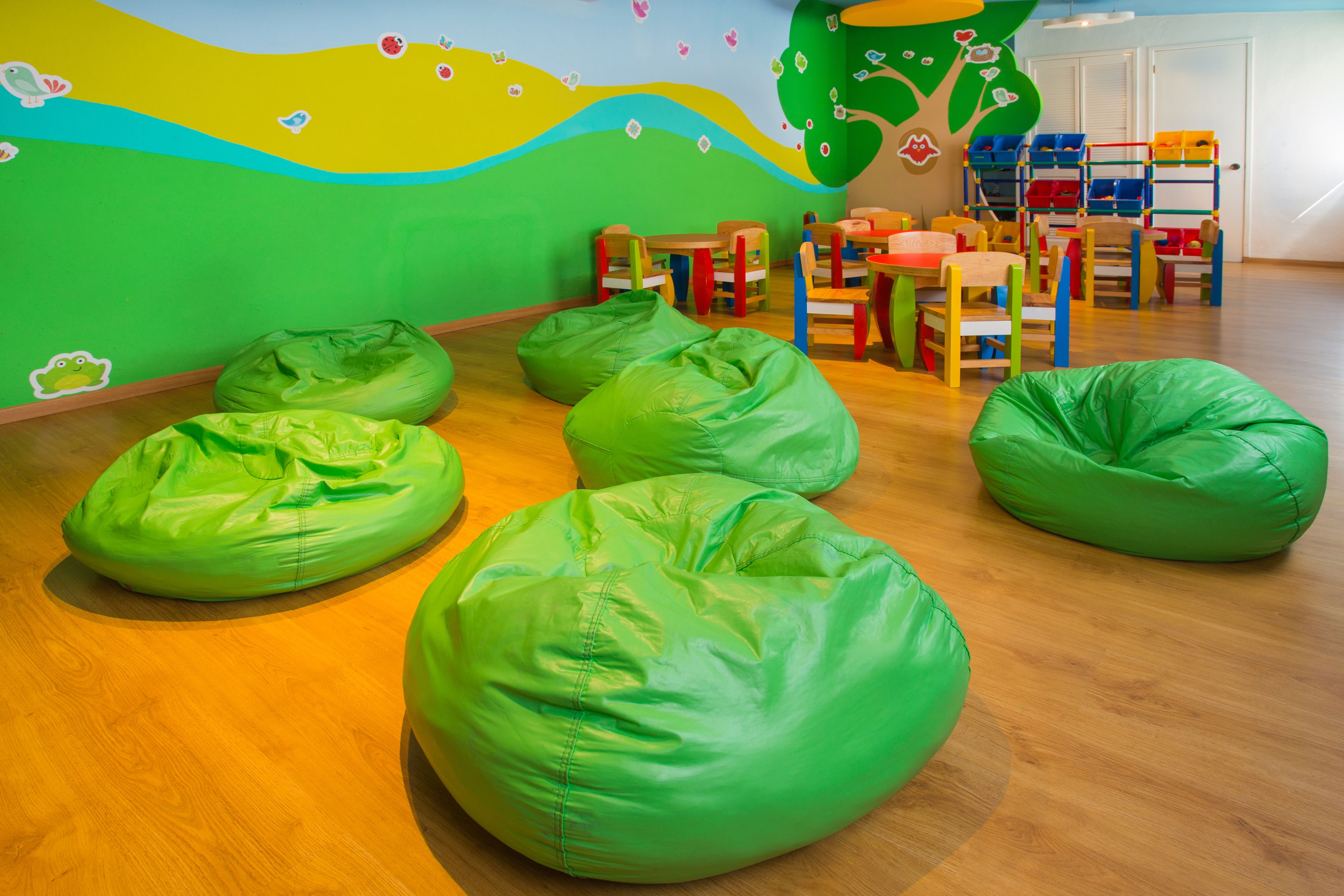 A children's playroom with green bean bags, colorful chairs, and a mural on the wall.
