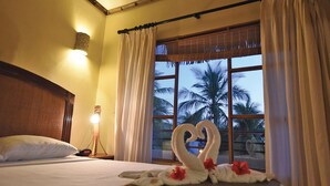 A hotel room with a bed, a nightstand with a lamp, and a window with curtains. - Canciones del Mar (Jaco)