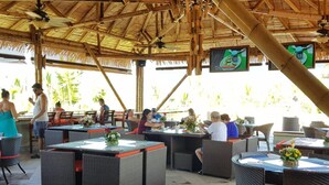 An outdoor restaurant with wicker furniture, a thatched roof, and a TV screen. - Canciones del Mar (Jaco)