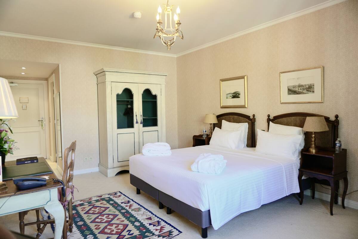 Una habitación de hotel con una cama grande, dos mesitas de noche, un armario, un escritorio con silla y una alfombra estampada.