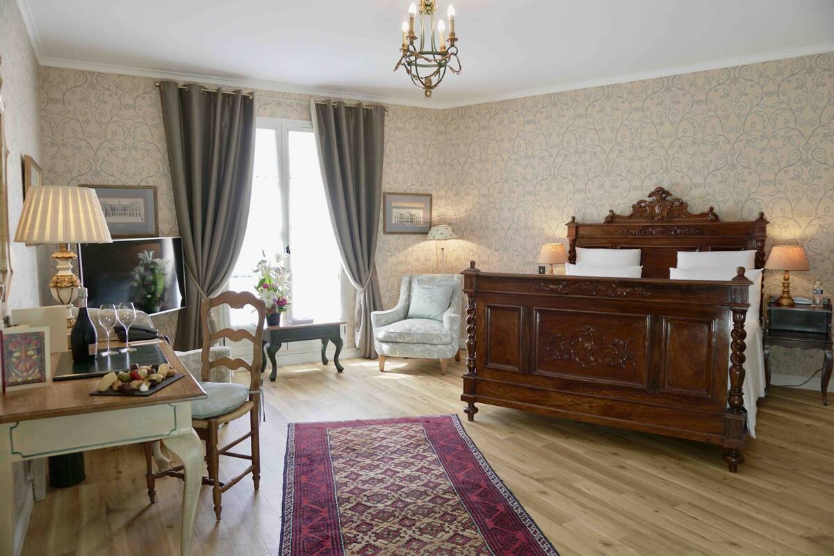 Una habitación tradicional con una cama de madera, un escritorio con lámpara, una silla y una alfombra estampada.