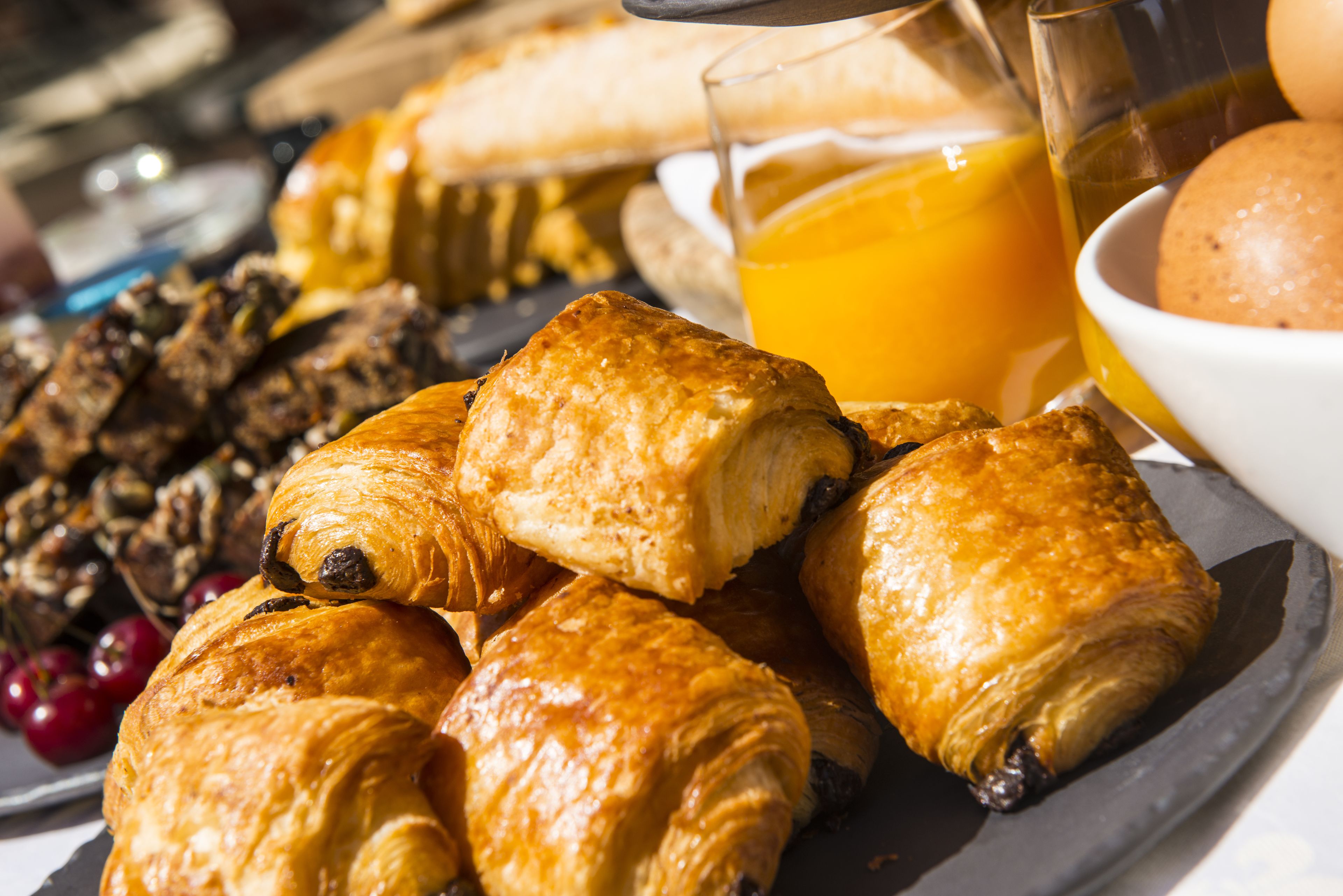 A breakfast plate with croissants, a glass of orange juice, and a bowl of fruit.