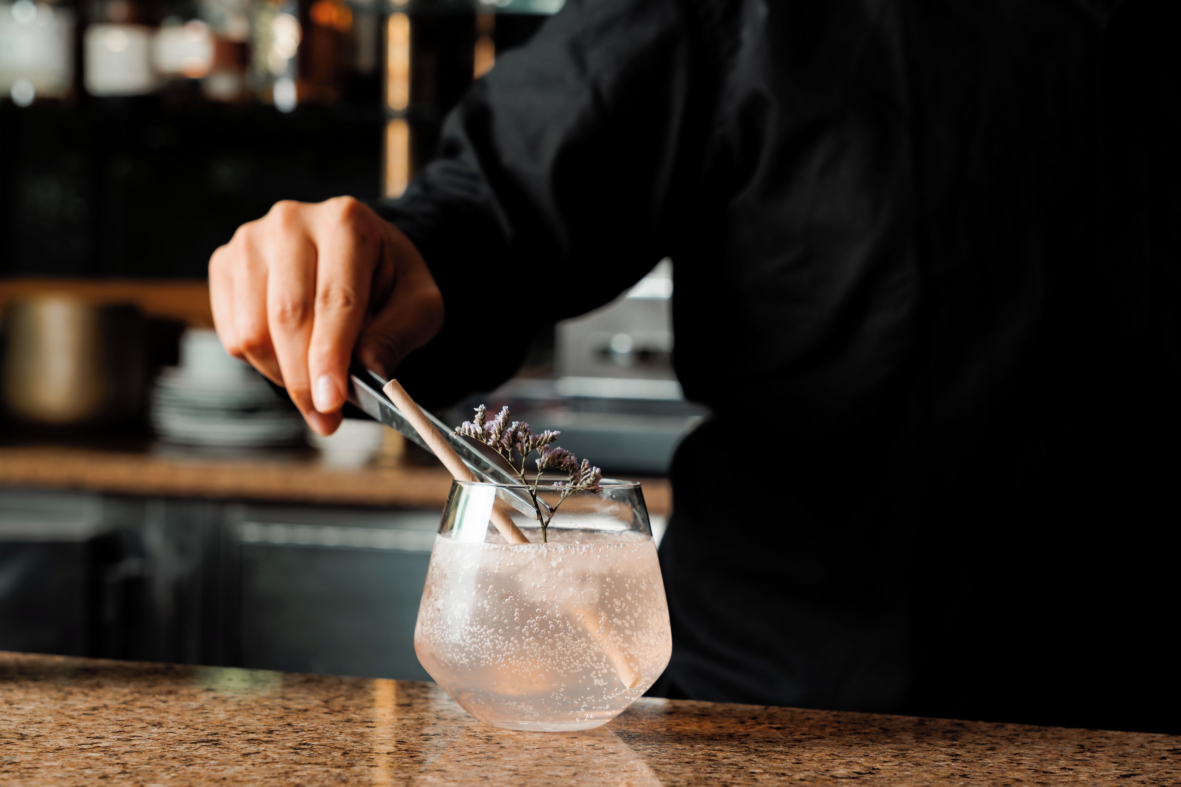 A person pouring a drink into a glass with a floral garnish.