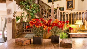 A staircase with wooden balusters, a potted plant with red flowers, and a vintage suitcase on the floor.