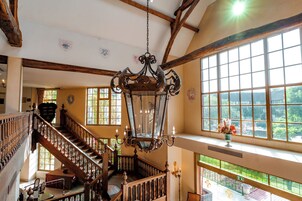Un interior espacioso con una escalera imponente, un candelabro y amplias ventanas que ofrecen vistas al exterior.