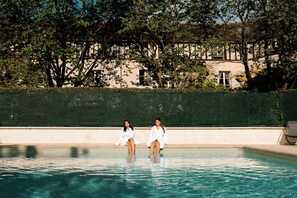 Deux personnes dans une piscine, avec un bâtiment et des arbres en arrière-plan.