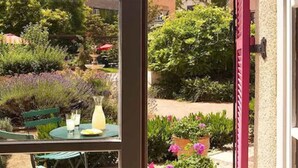 A patio with a table and chairs, surrounded by lush greenery and flowering plants.