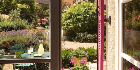 Un patio con mesa y sillas, rodeado de exuberante follaje y plantas con flores.