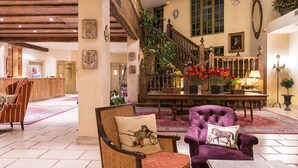 A spacious lobby with a wooden staircase, a reception desk, and a seating area with a purple armchair and a wicker chair.