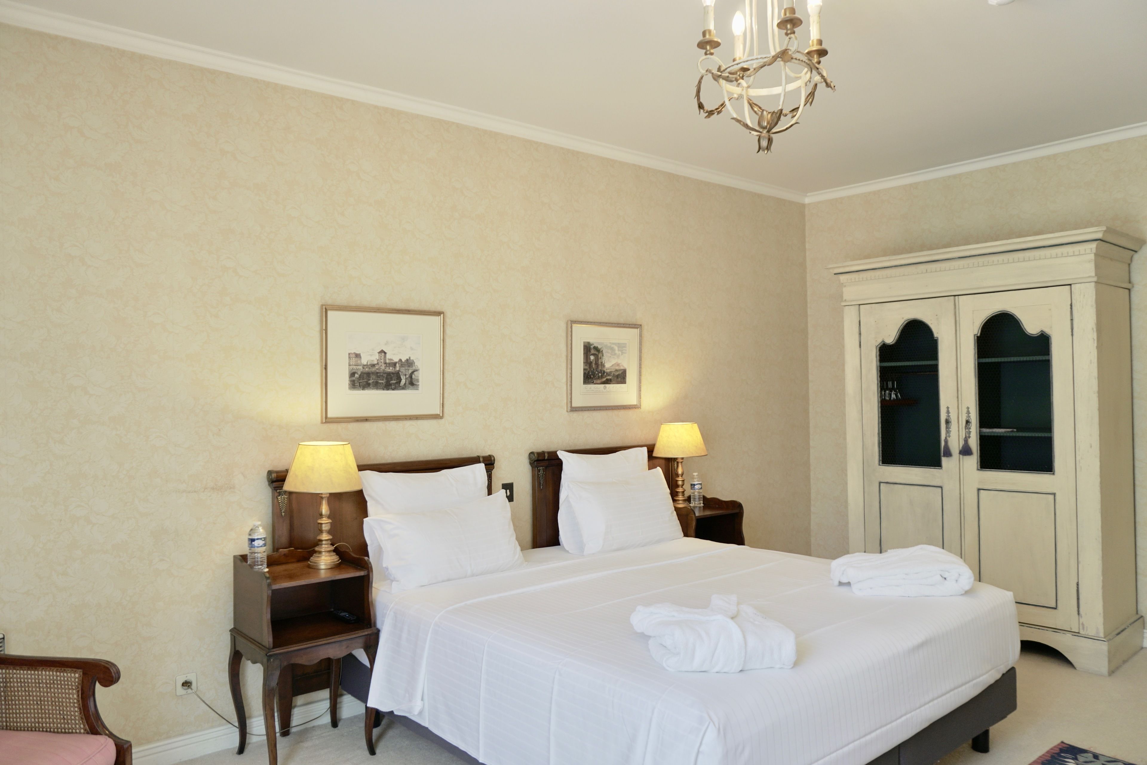 Een hotelkamer met een groot bed, twee nachtkastjes met lampen, een kledingkast en ingelijste foto's aan de muur.