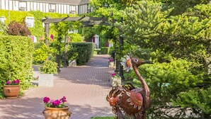 A pathway leading to a building with a covered entrance, surrounded by greenery and potted plants.