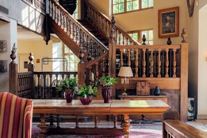 Un magnifique escalier avec des balustrades en bois, un lustre et une table agrémentée de compositions florales.