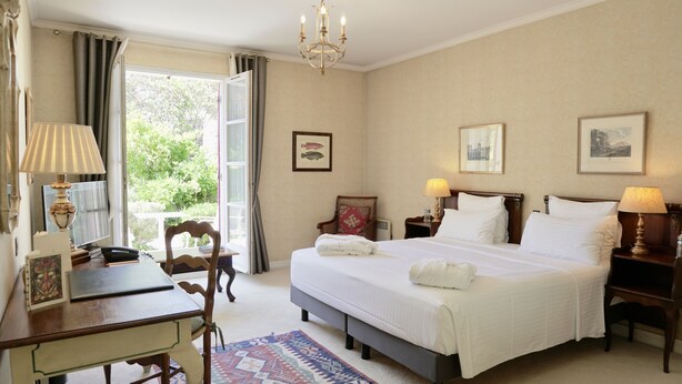 A hotel room with a large bed, bedside tables with lamps, a desk, a chair, and a view of the outdoors.