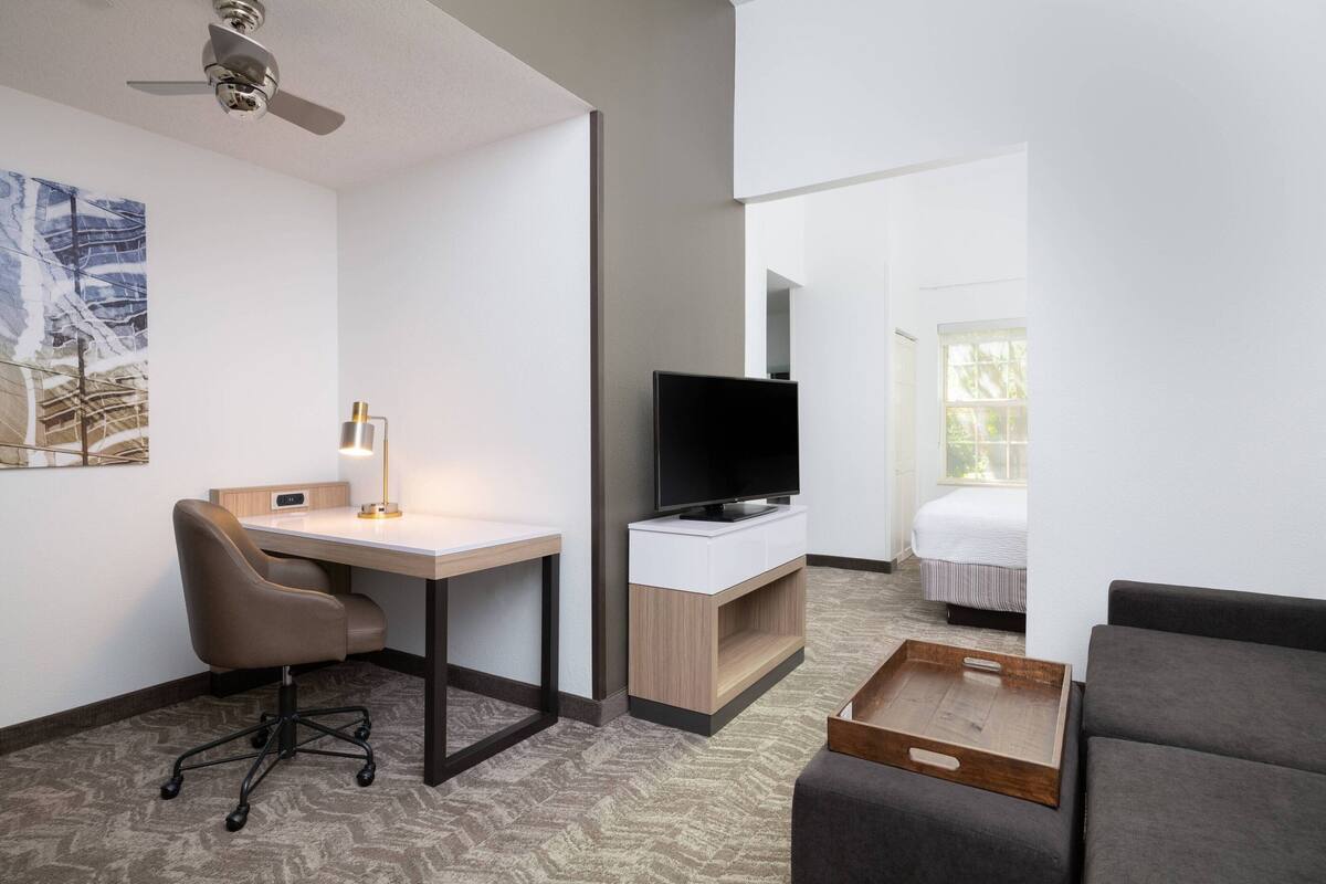 A hotel room with a desk, chair, TV, bed, and a sofa.