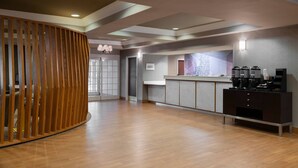 A modern reception area with a wooden partition, a coffee station, and a view of the cityscape through the window. - Springhill Suites by Marriott Williamsburg (Williamsburg)