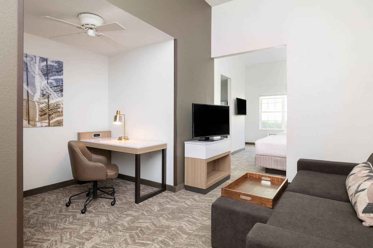 A modern hotel room with a desk, chair, flat-screen TV, sofa, and a bed.