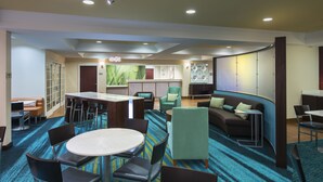 A hotel lobby with a round dining table, several chairs, a sofa, and a kitchen area in the background. - Springhill Suites by Marriott Williamsburg (Williamsburg)