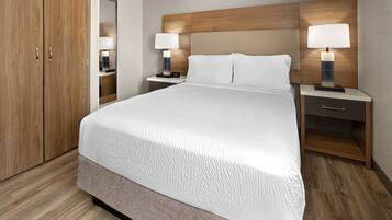 A hotel room with a large bed, wooden headboard, two bedside tables with lamps, a nightstand, and a wardrobe.