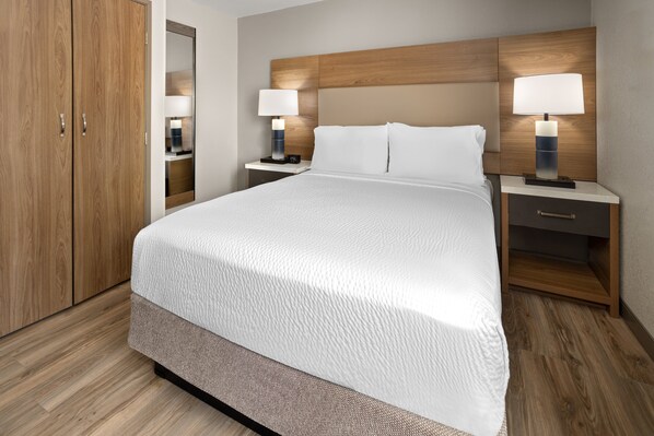 Une chambre d’hôtel avec un grand lit, une tête de lit en bois, deux tables de chevet avec des lampes, une table de nuit et une armoire.