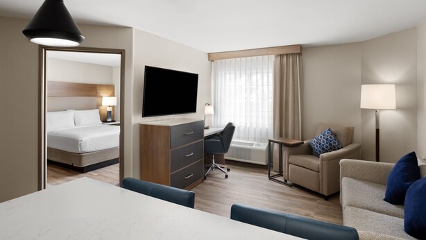 A hotel room with a bed, desk, TV, and seating area.