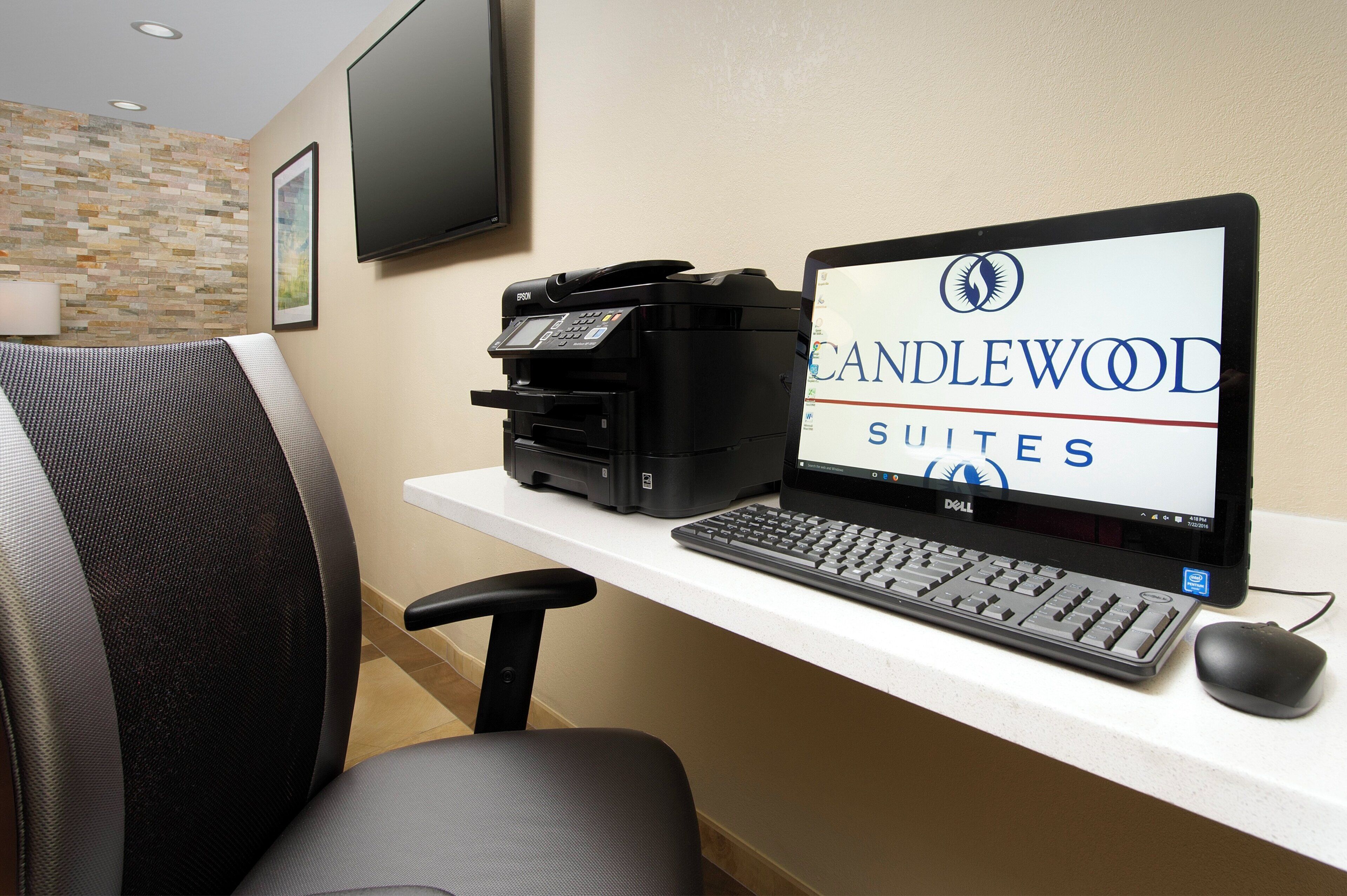 Mostrador de recepción de hotel con monitor que muestra 'CANDLEWOOD SUITES', una impresora y un teclado.