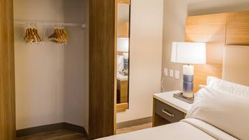 A hotel room with a bed, bedside table, lamp, and a wooden wardrobe with hanging clothes.