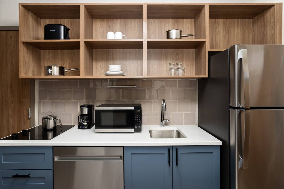 Une cuisine moderne avec des meubles en bois, un réfrigérateur en acier inoxydable, un four à micro-ondes et une machine à café.