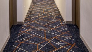 A hotel hallway with a patterned carpet, doors on both sides, and a ceiling light.