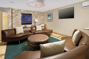 Ein modernes Wohnzimmer mit einem Ecksofa, einem runden Ottomanen und einem flachbildfernseher an der Wand.