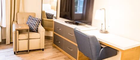 A hotel room with a desk, chair, television, and a mirror.