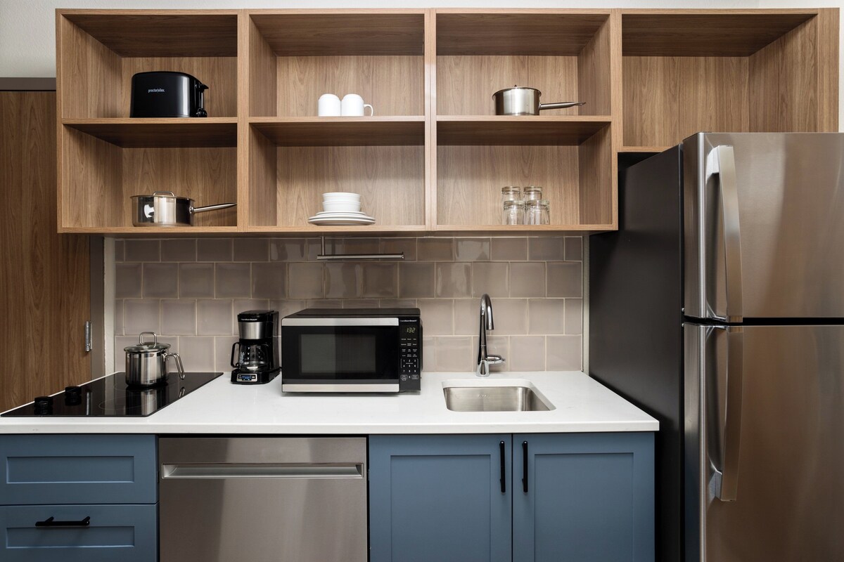 Eine moderne Küche mit Holzschränken, einem Edelstahlkühlschrank, einer Mikrowelle und einer Kaffeemaschine.