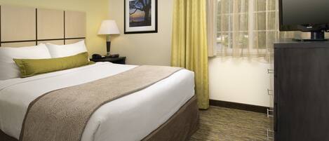 A hotel room with a bed, a nightstand, a lamp, a television, and a window with curtains.