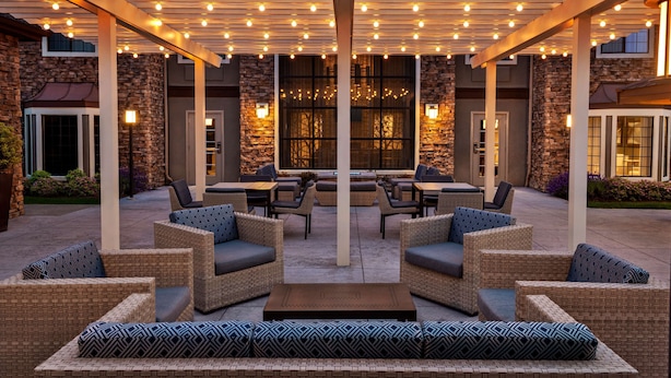 Une terrasse extérieure avec des meubles en osier et une pergola décorée de guirlandes lumineuses.
