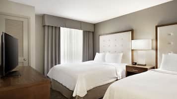 A hotel room with two beds, a television on a wooden dresser, and a nightstand with a lamp.