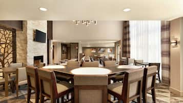 A spacious dining area with a large round table surrounded by upholstered chairs, a stone accent wall, and a flat-screen TV mounted above the fireplace.