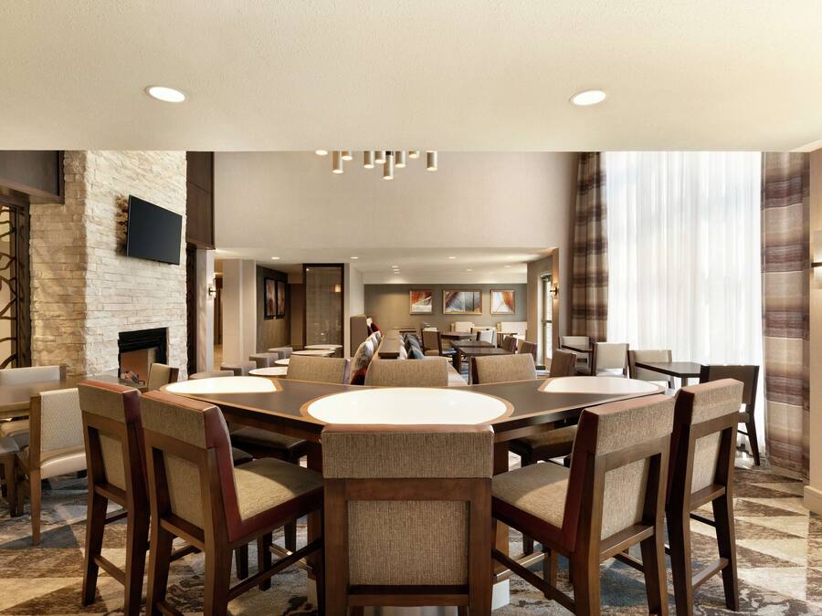 A spacious dining area with a large round table surrounded by upholstered chairs, a stone accent wall, and a flat-screen TV mounted above the fireplace.