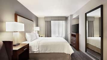 Habitación de hotel con una cama grande, un escritorio con lámpara, televisor y espejo.