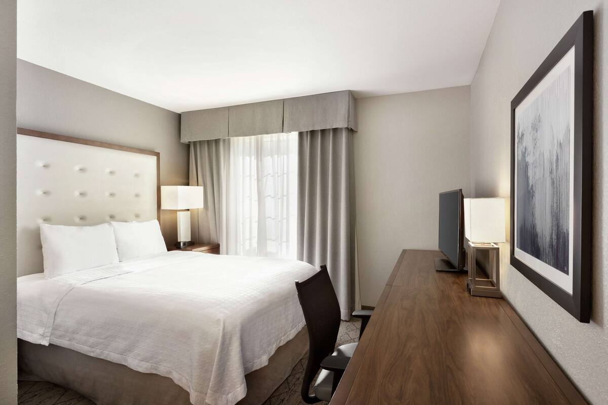 A hotel room with a large bed, a desk, a chair, a television, and a framed picture on the wall.