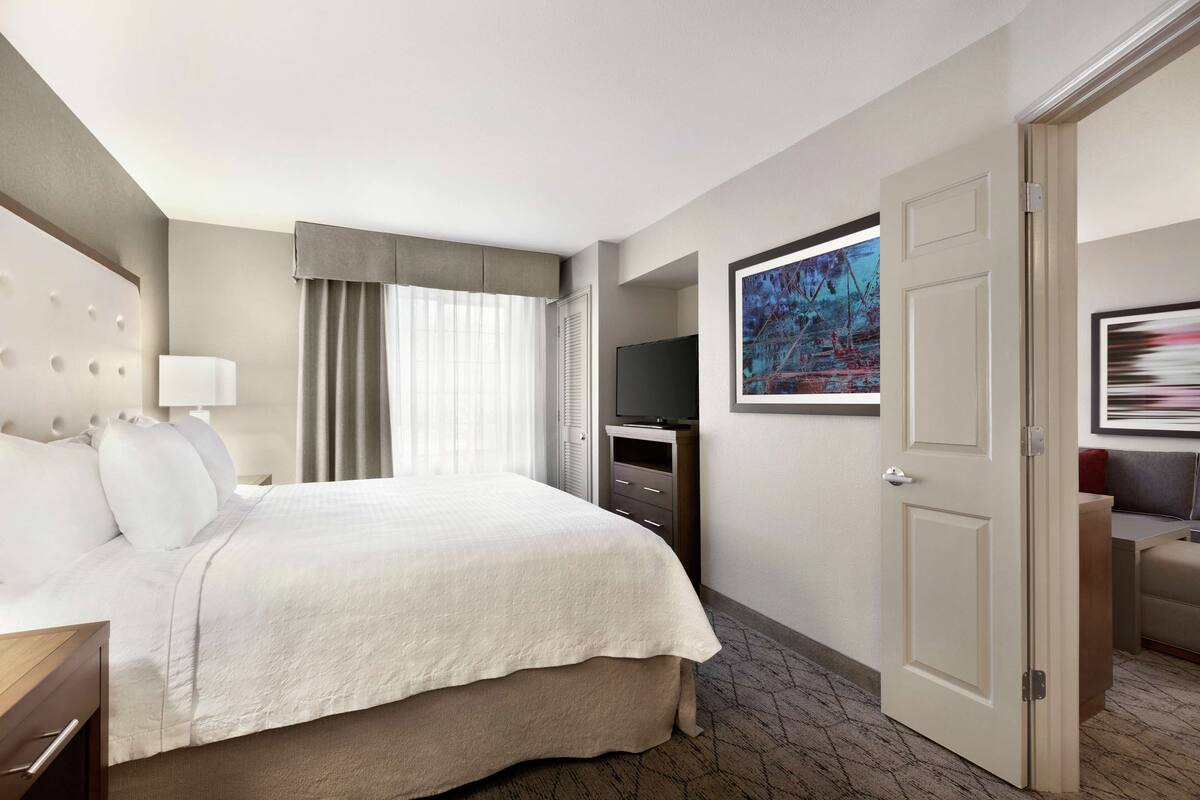 A hotel room with a large bed, a television, a desk, and a door.