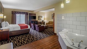 Habitación de hotel con cama, escritorio, silla, sofá, televisión, lámpara de escritorio y baño con bañera y ducha.